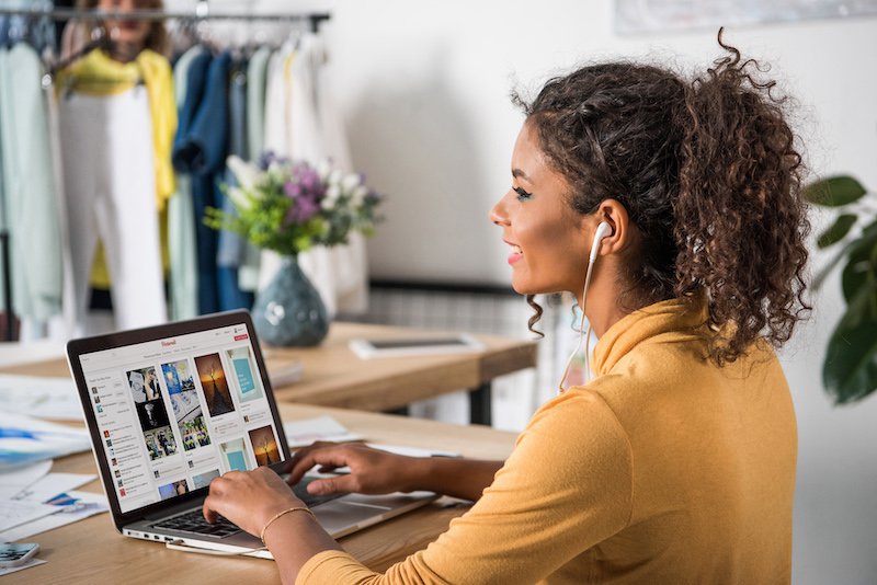 frumoasă tânără afro-americană zâmbitoare în căști folosind laptop