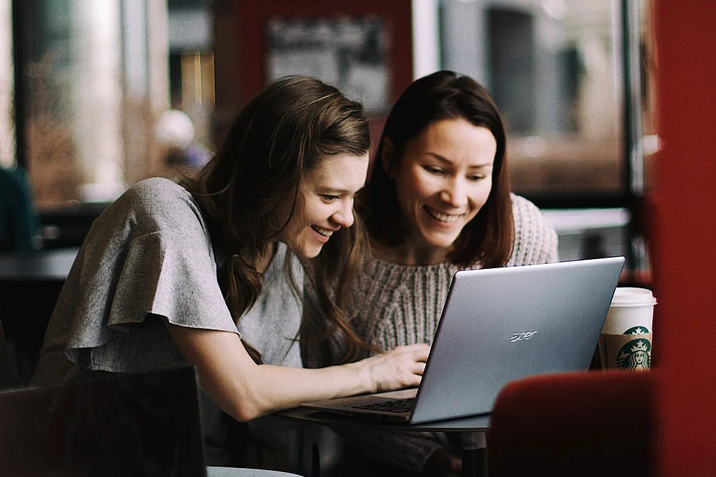 Doi oameni care se uită la ecranul unui laptop într-o cafenea