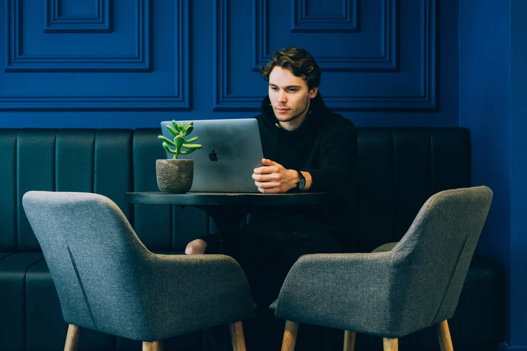 persoană care stă într-o cameră cu un laptop și un perete albastru în spate, stând pe un scaun albastru