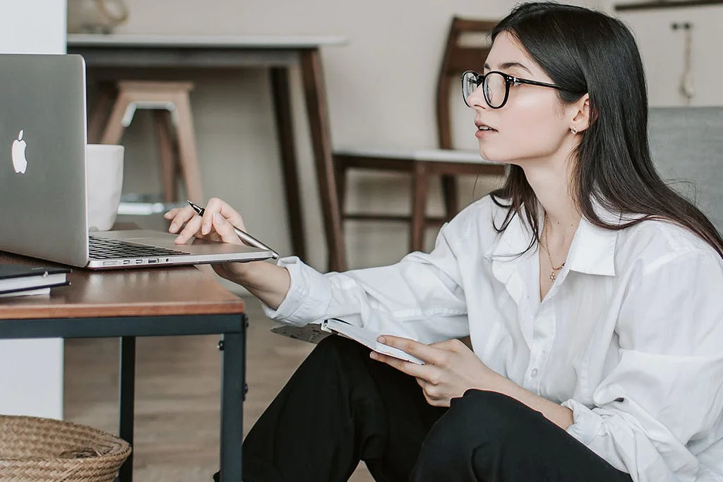 Persoană așezată pe podea care lucrează la un laptop așezată pe o măsuță de cafea