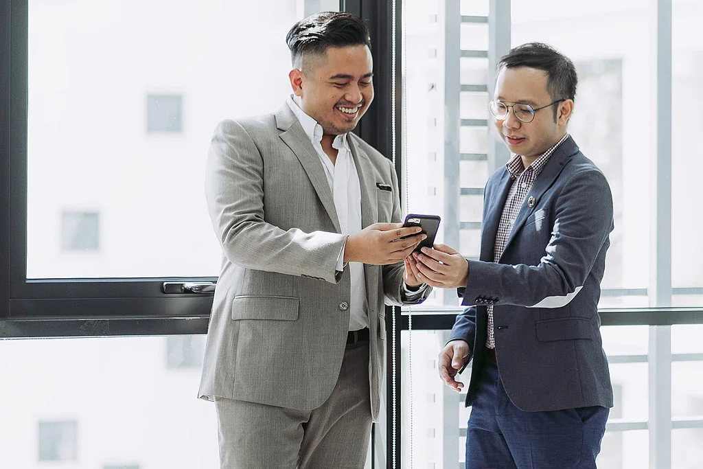 doi oameni care se uită împreună la un telefon zâmbind