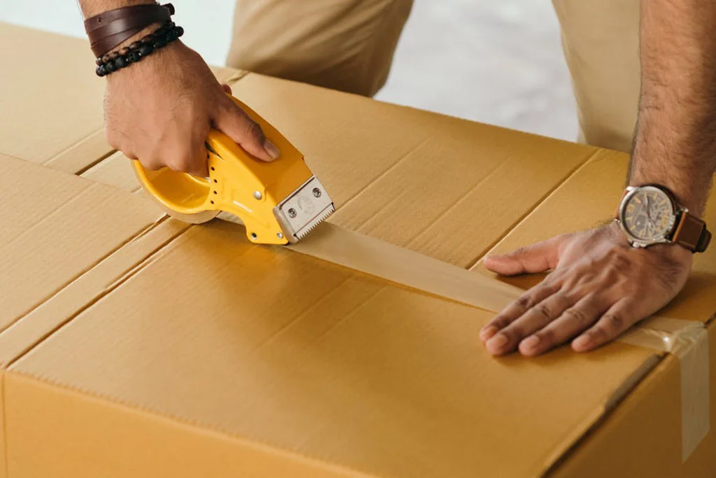 Persona che stende il nastro sulla parte superiore di una scatola