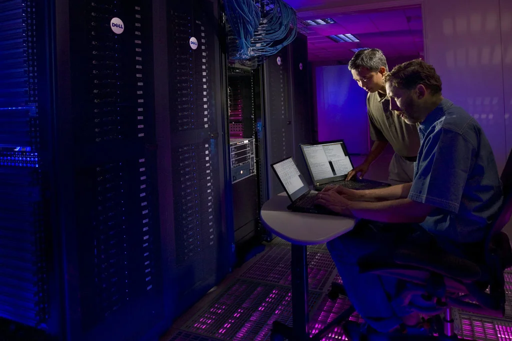 Due persone che lavorano su un computer seduti accanto a uno stack di server