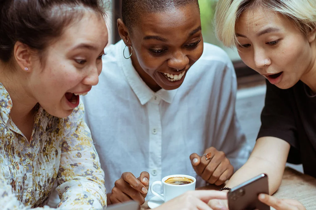 Trei oameni care se uită la un telefon râzând și zâmbind