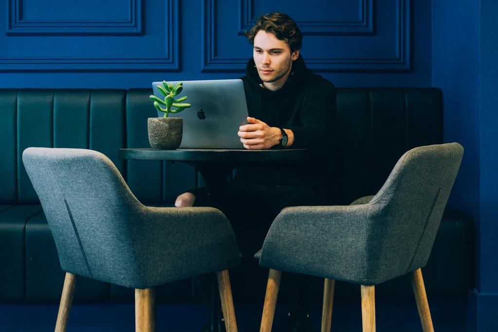 Persoană care stă la masă și lucrează la un laptop