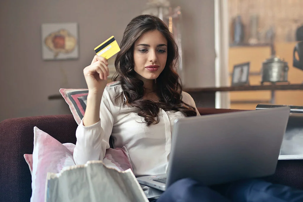 Persoană care stă pe o canapea cu un card de credit și cumpără ceva de pe un computer
