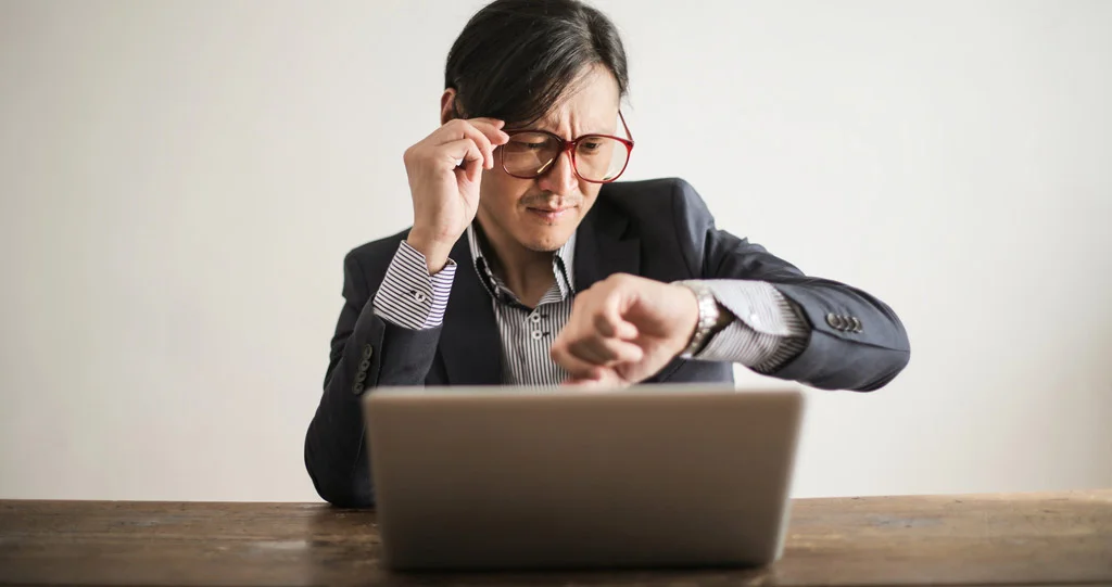 شخص ينظر إلى ساعته وهو ينظر إلى الكمبيوتر