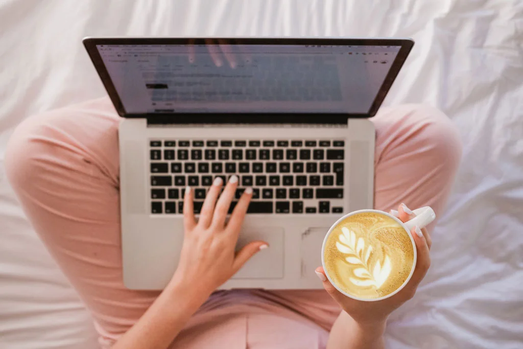 Persona in possesso di un caffè che lavora su un laptop