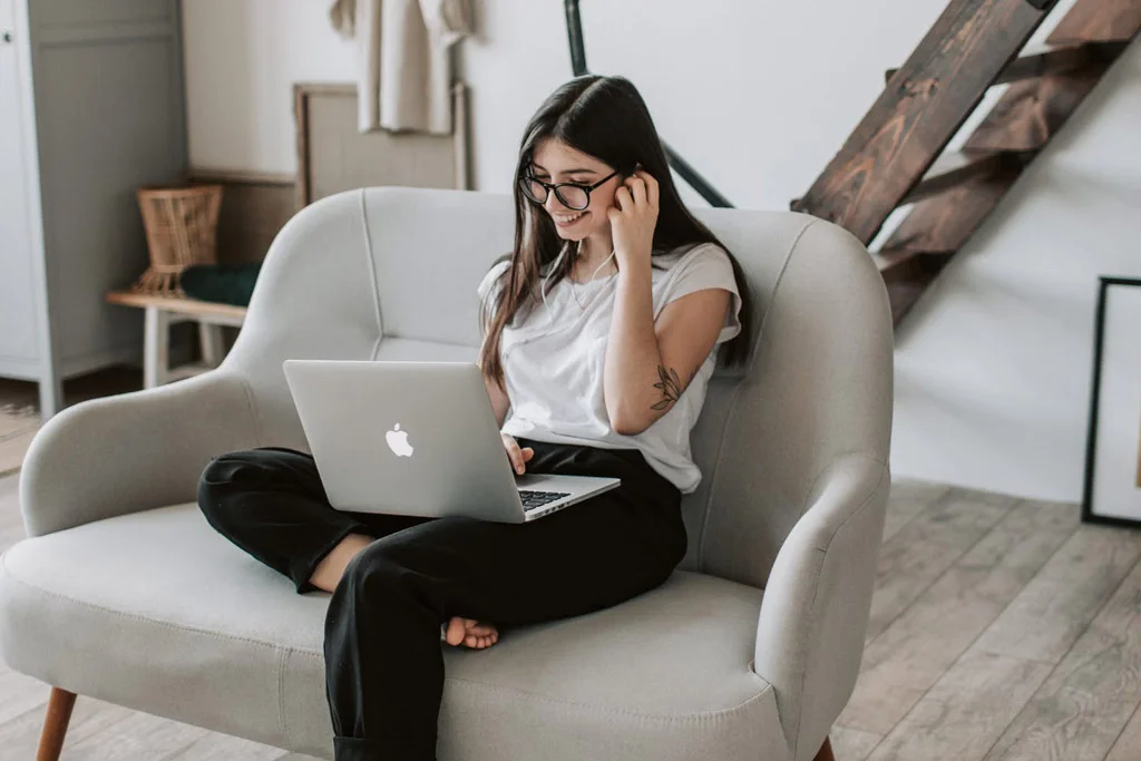 Persona seduta su un divano che sorride e lavora al computer