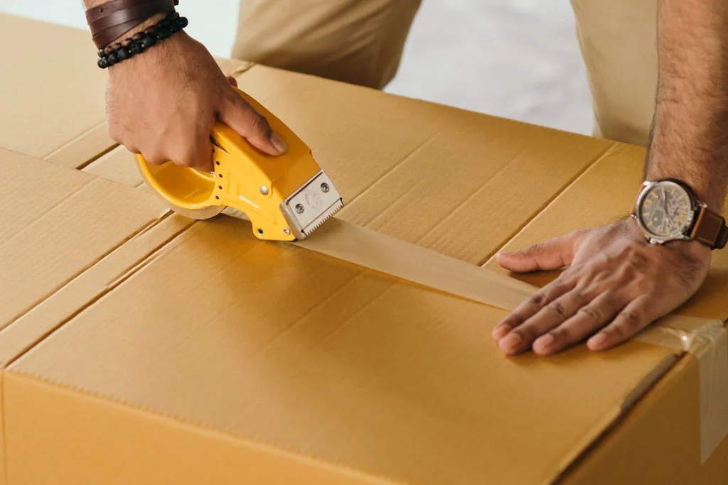 在纸板箱上拉伸胶带的人