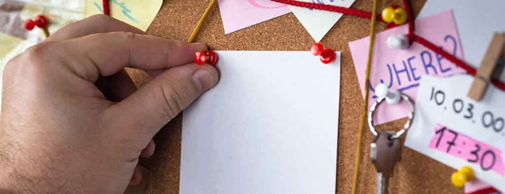 una nota adesiva vuota appuntata su una bacheca di sughero