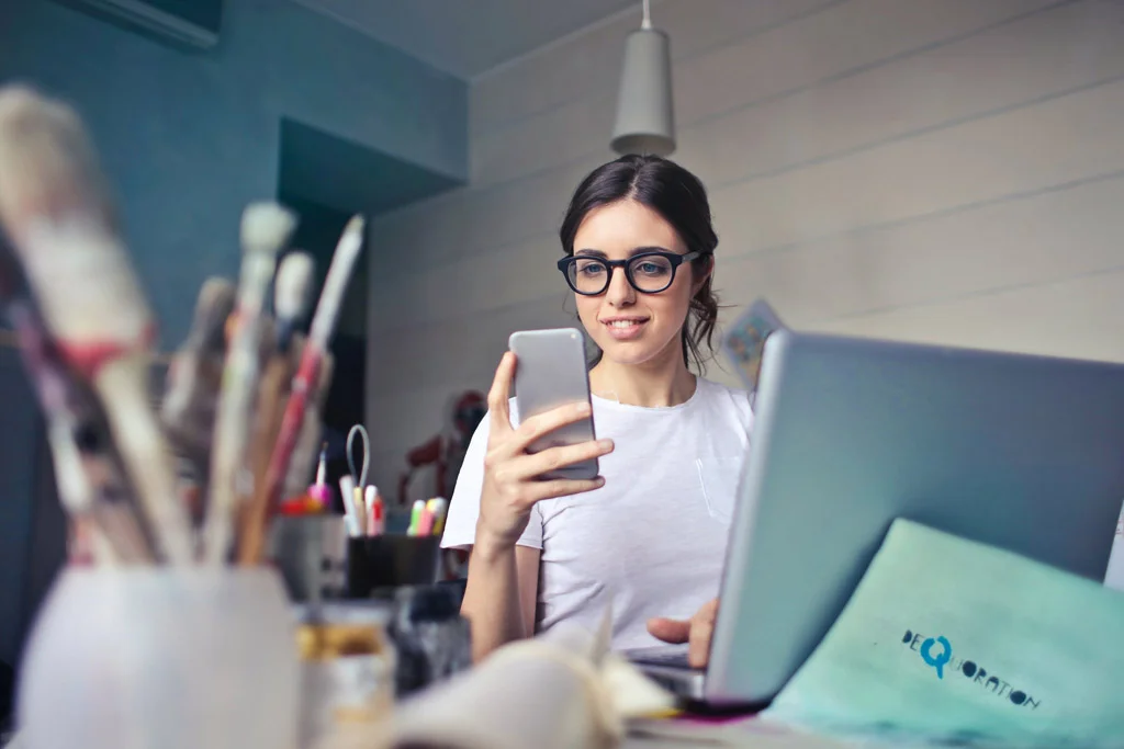 bir bilgisayar kullanırken aynı zamanda telefona bakan bir kişi