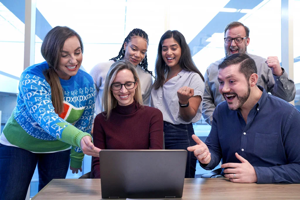 bir bilgisayarın etrafında mutlu ve heyecanlı görünen bir grup insan
