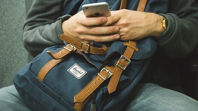 seseorang dengan ransel menggunakan smartphone-nya