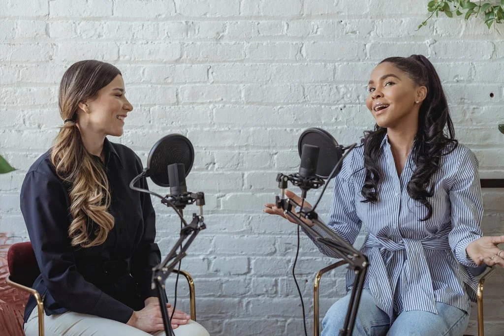 Zwei Personen sitzen nebeneinander und sprechen in Mikrofone