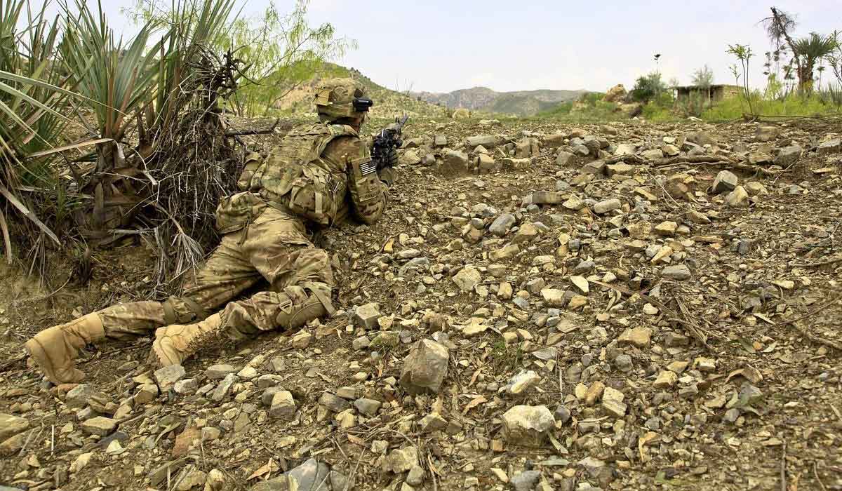 苔むした岩の上を這う兵士は、オリーブグリーンの制服を着てカモフラージュされています。