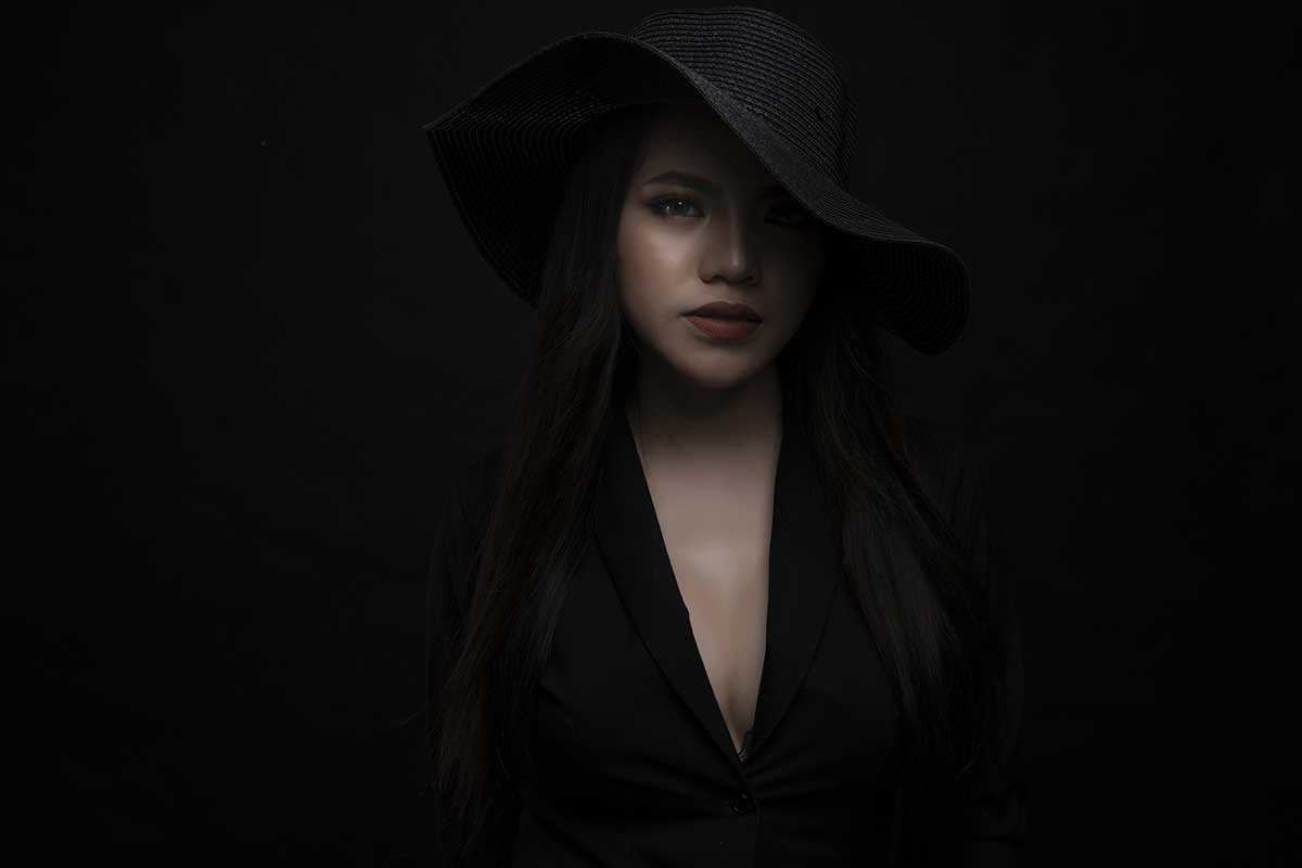 Frau mit schwarzem Hut auf schwarzem Hintergrund sieht mysteriös und raffiniert aus.