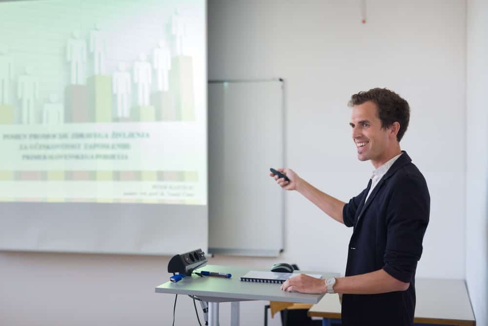 Un homme avec un sélecteur PowerPoint le pointe sur l'écran du projecteur pendant qu'il présente pendant la réunion.
