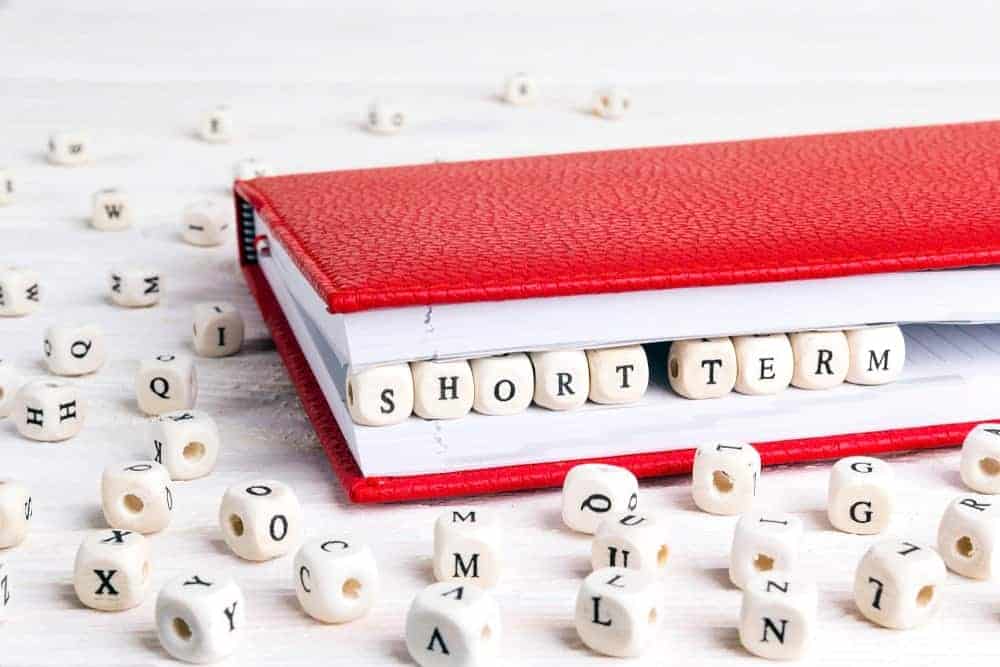 Les mots "court terme" épelés en dés de scrabble entre les pages d'un cahier rouge.