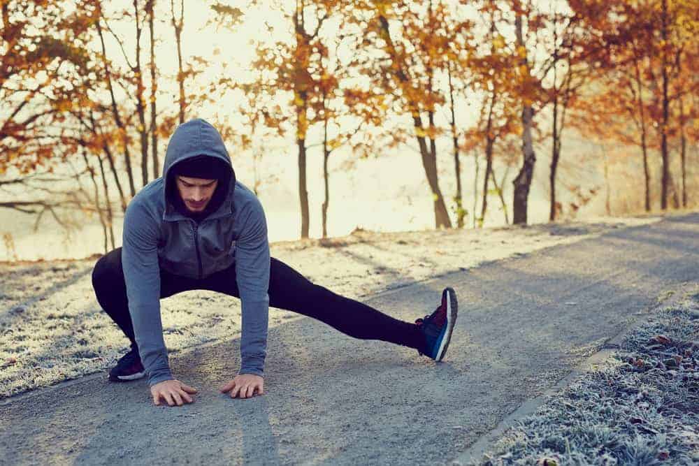 Un homme portant une veste à capuche faisant un étirement à l'extérieur.