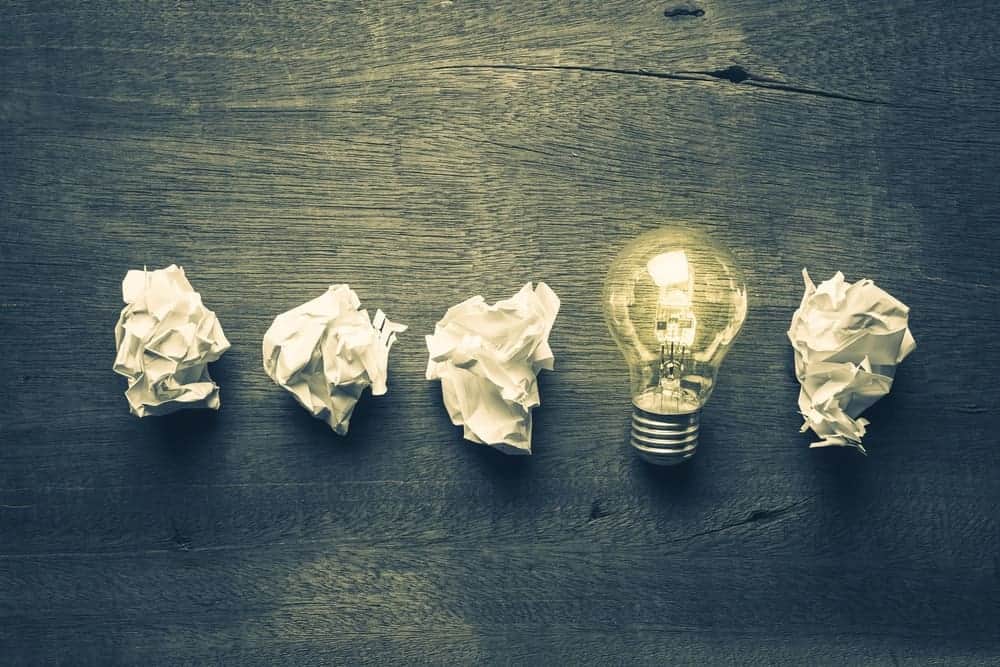 Une ampoule allumée entourée de papier blanc froissé sous une forme linéaire sur un bureau en bois.