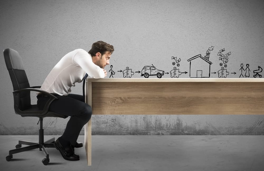 Un homme s'appuie sur une table en bois alors qu'il regarde droit devant lui avec des croquis d'objectifs familiaux au-dessus de la surface de la table.
