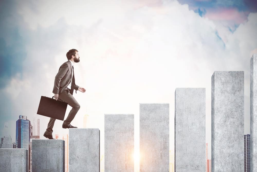 Un homme d'affaires en costume portant une valise alors qu'il grimpe sur une échelle figurative.