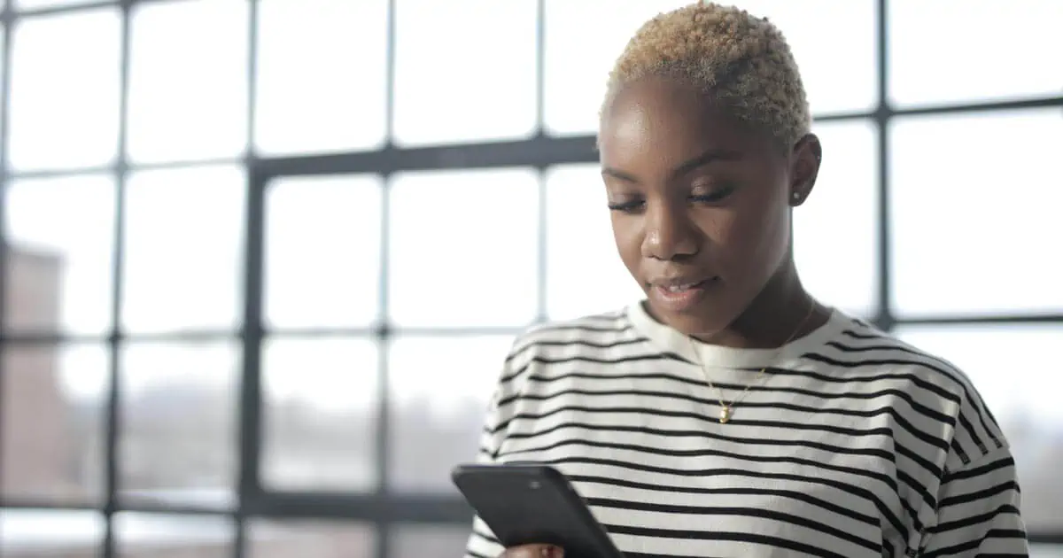 امرأة ترتدي قميصًا أبيض وأسود ياقة طاقم مخططة تحمل هاتفًا ذكيًا أسود