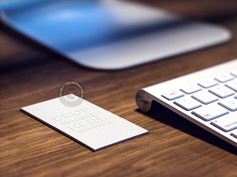MOCKUP OF A BUSINESS CARD LYING ON TOP OF A DESK AT A CREATIVE OFFICE