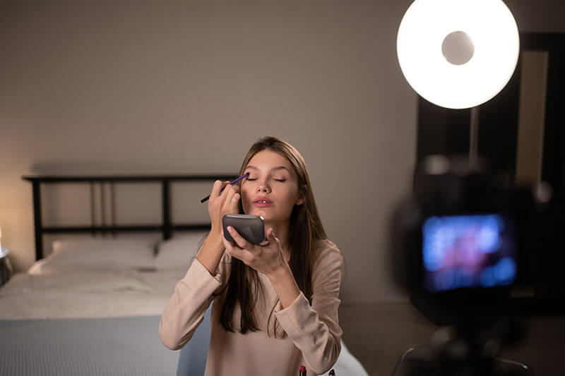 カメラのアイシャドウを適用する女性インフルエンサー