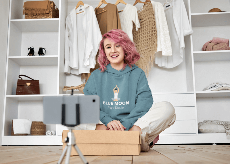 Pullover Hoodie Mockup di una donna con i capelli rosa che registra un live streaming di Unboxing
