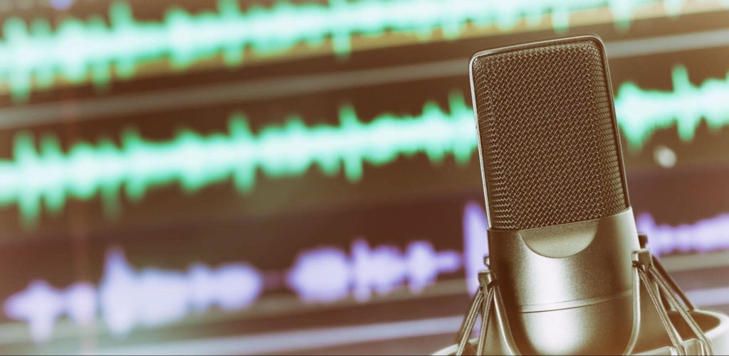 Uma imagem de perto de um microfone de estúdio e uma tela de computador executando um software de gravação em segundo plano.