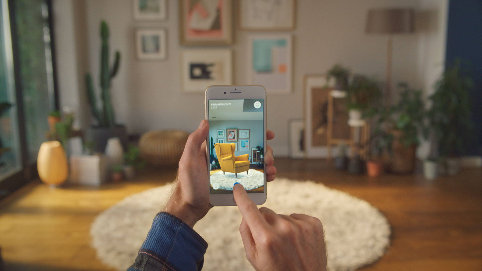 Aplikasi IKEA Place AR A smartphone held by its user. The screen captures the living room in the background with the addition of a lounge chair.