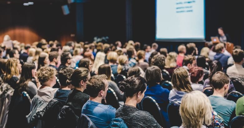 O audiență atinsă de rețelele sociale, adunată într-o sală pentru a participa la un eveniment.