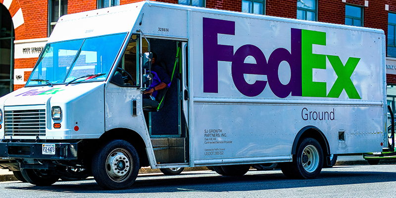 Un camion FedEx bianco con uomo di consegna all'interno, parcheggiato all'esterno di un edificio per uffici a Washington DC in una giornata di sole.