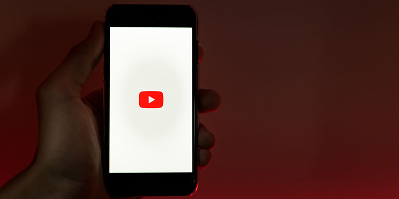 画面に YouTube ロゴが表示された携帯電話を持つ手