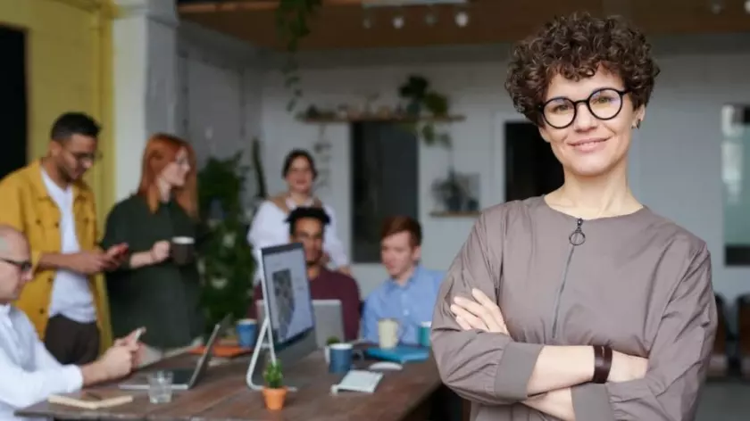Une femme à lunettes debout devant un groupe de personnes.