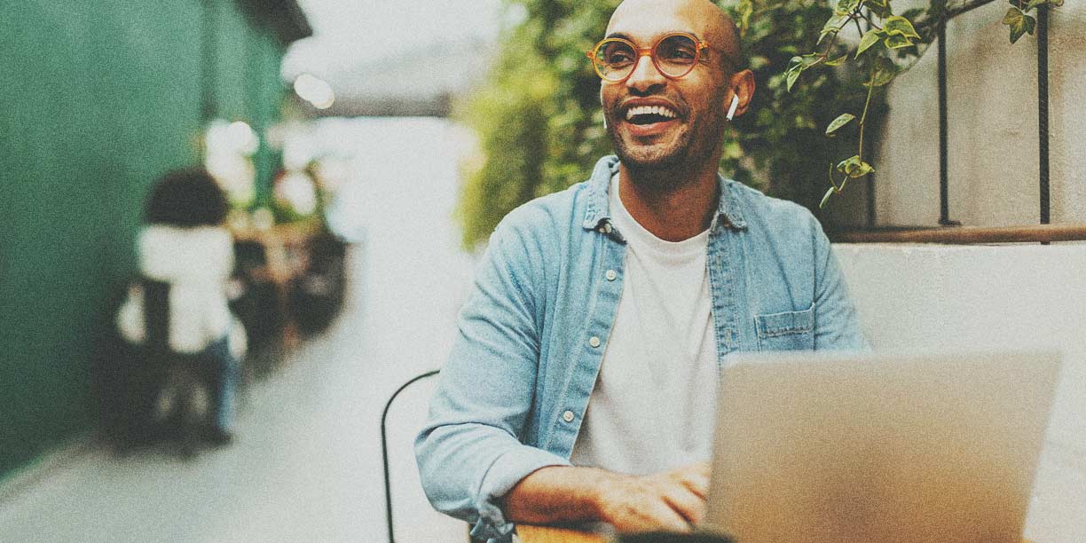Homem de camisa azul trabalhando em um laptop e sorrindo