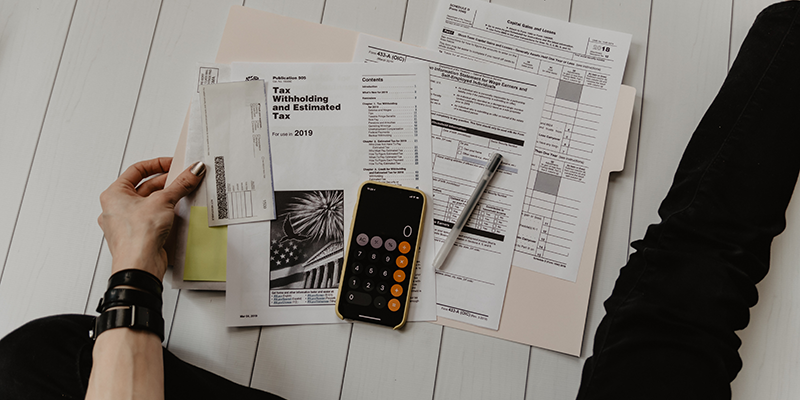 Diferentes formularios de impuestos, un bolígrafo y una calculadora sobre una plataforma de madera blanca