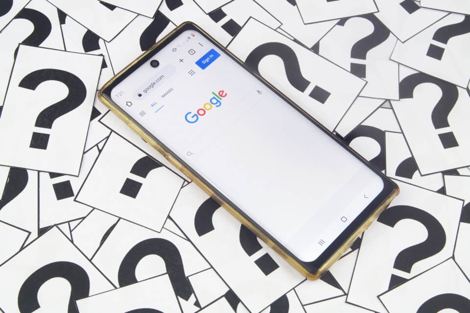 Un telefono cellulare sulla home page di Google circondato da punti interrogativi