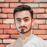 Ghasif Hermain, der Autor dieses Artikels, steht in einem weißen Hemd vor einer Ziegelwand. Ghasif Hermain, the author of this article, in a white shirt standing in front of a brick wall.