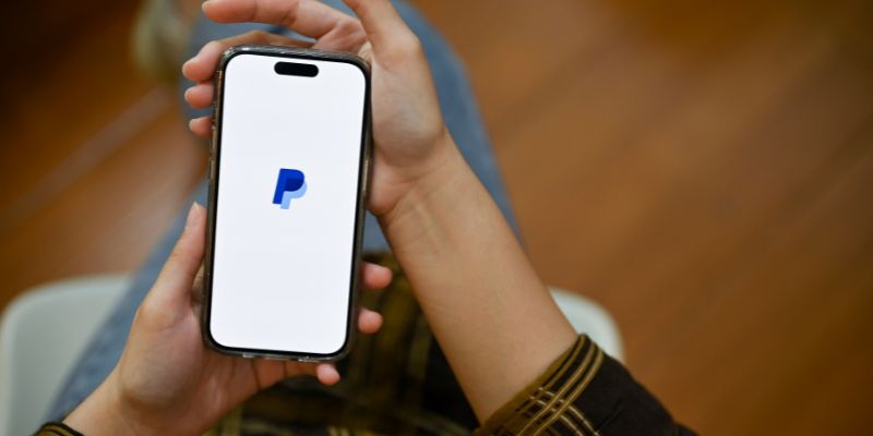 Hände halten ein Smartphone mit einem Paypal-Logo