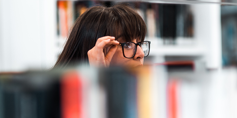 Uma mulher usando óculos pretos verificando livros em uma biblioteca