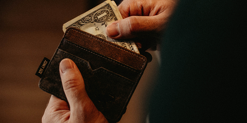 Ręka usuwająca banknoty dolarowe z brązowego portfela
